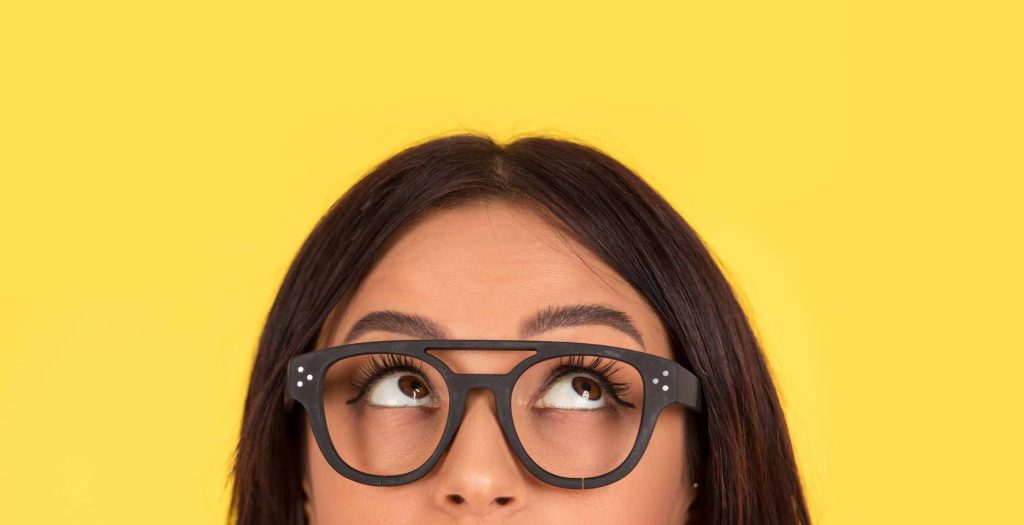 closeup portrait headshot cropped face above lips of cute happy woman in glasses looking up isolated on yellow studio wall background with copy space above head. Human face expressions, emotions
