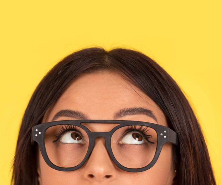 closeup portrait headshot cropped face above lips of cute happy woman in glasses looking up isolated on yellow studio wall background with copy space above head. Human face expressions, emotions