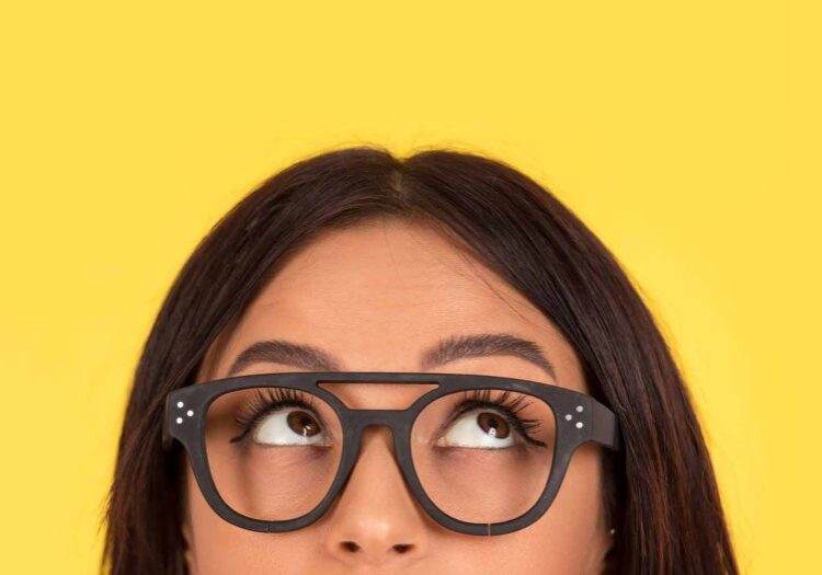 closeup portrait headshot cropped face above lips of cute happy woman in glasses looking up isolated on yellow studio wall background with copy space above head. Human face expressions, emotions